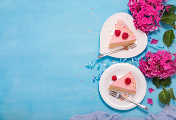 Two pieces of festive cake with flowers on blue background, flat lay copy space