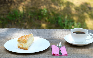 Close up front view of a piece of classic tradiional German bee sting cake (Biienenstich) with caramelized almond. A cup of black coffee is in the top right corner.