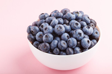 Fresh blueberry in white bowl on  pink background. side view.