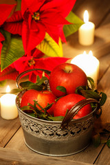 Silver bucket of red ripe apples among candles on rustic wooden table.