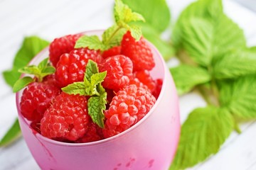 Fresh,ripe raspberries in a Cup and green raspberry leaves on a white background.