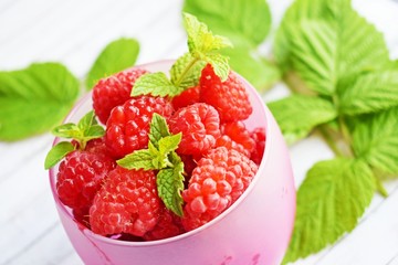 Fresh,ripe raspberries in a Cup and green raspberry leaves on a white background.