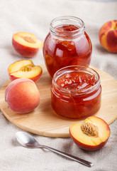 Peach jam in a glass jar with fresh fruits on gray concrete background. side view.
