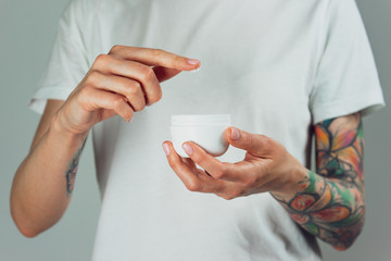 Female tattooed hands holding a jar of cream. Finger with a drop of white cream