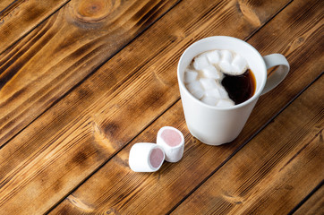 Marshmallow and cup with black coffe on wooden background