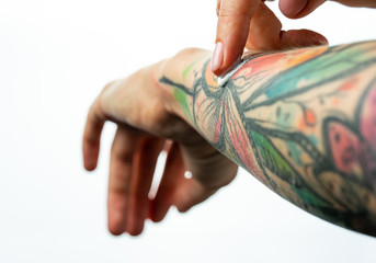 Female tattooed hands hold a jar of cream. Fingers apply cream to skin. Close up
