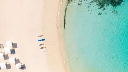 Beach umbrellas and deck chairs on the white beach. White sandy beach and clear turquoise lagoon, top view.