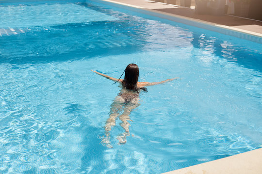 Outdoor picture of dark haired woman back view, relaxing in swimming pool, swimming professionally, having luxury rest, enjoying time at hotel spa resort, improving her swimming skills. Rest concept.