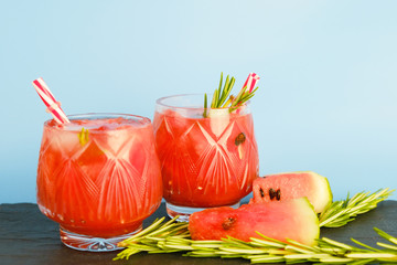 Two glasses of watermelon refreshing summer drink. Watermelon juice with rosemary on blue background.