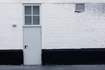 White and black facade of a brick building with metal door and window