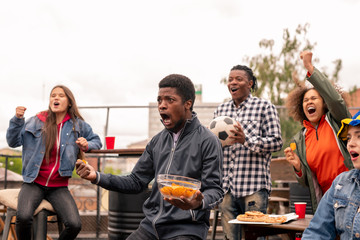 Multi-ethnic group of ecstatic youth with snack shouting during broadcast