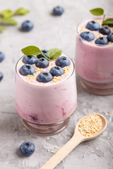 Yoghurt with blueberry and sesame in a glass and wooden spoon on gray concrete background. side view.