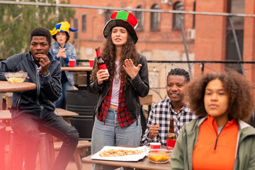 Group of young intercultural fans eating chips and pizza during match broadcast