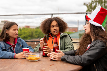 Young multi-ethnic female football fans having beer with chips by chat