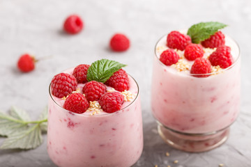 Yoghurt with raspberry and sesame in a glass and wooden spoon on gray concrete background. side view.