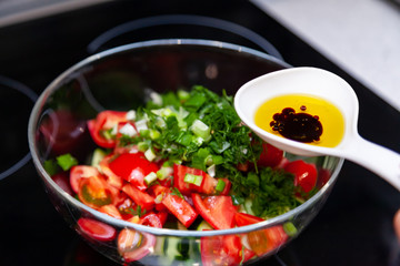 Preparation of salad from fresh vegetables, cucumbers, tomatoes and greens with a white plastic spoon containing a salad dressing made from olive oil, balsamic vinegar and soy bean sauce