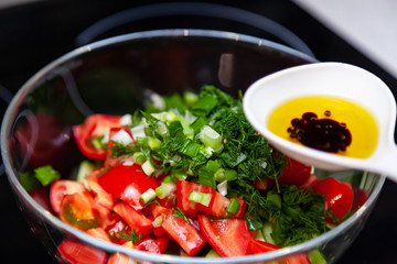 Preparation of salad from fresh vegetables, cucumbers, tomatoes and greens with a white plastic spoon containing a salad dressing made from olive oil, balsamic vinegar and soy bean sauce