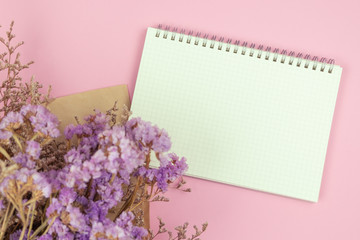 Top view of empty notebook and flower bouquet on pastel pink background