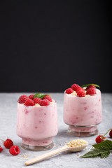 Yoghurt with raspberry and sesame in a glass and wooden spoon on gray and black background. side view.