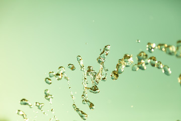 Water droplets frozen in the air with splashes and chain bubbles on a green isolated background in nature. Clear and transparent liquid symbolizing health and nature.