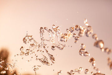 Water droplets frozen in the air with splashes and chain bubbles on a golden and bronze isolated background in nature. Clear and transparent liquid symbolizing health and nature.