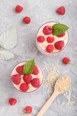 Yoghurt with raspberry and sesame in a glass and wooden spoon on gray concrete background. top view.