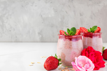 overnight oats or oatmeal porridge with fresh strawberries and mint in glasses with rose flowers on white marble table