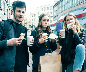 lifestyle and people concept: two girls and guy eating fast food on city street together having...