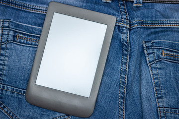 An e-reader hidden in a pocket of jeans pants. Close-up with selective focus. Copy space. Training and technology concept