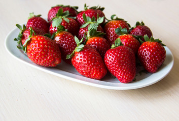 Fresh strawberries on a white plate on a wooden light background, copy space. Strawberry background. Sweet, juicy, ripe strawberries. Harvest of organic local  strawberries. Healthy food with vitamins