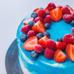 Close-up festive blue and white cake decorated with fruits: strawberries, raspberries, blueberries. Cake for birthday, holiday and anniversary