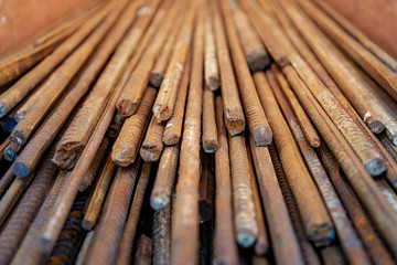 Close up selected focus view stack of straight old rusty high yield stress deformed reinforcement steel or iron bars. Background horizontal random pattern of deformed iron bars. 