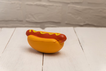 Artificial plastic hot dog toy on white wooden background with copy space. Harmful plastic food concept. Unhealthy eating