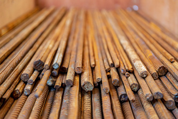 Close up selected focus view stack of straight old rusty high yield stress deformed reinforcement steel or iron bars. Background horizontal random pattern of deformed iron bars. 