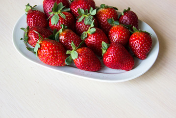 Fresh strawberries on a white plate on a wooden light background, copy space. Strawberry background. Sweet, juicy, ripe strawberries. Harvest of organic local  strawberries. Healthy food with vitamins