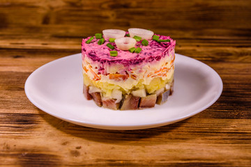 White plate with russian traditional new year salad herring under fur coat on wooden table