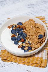 bowl of healthy wholegrain flakes, yogurt and blueberries, vertical