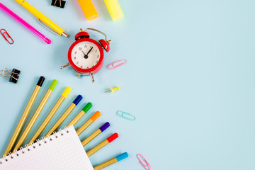 School supplies on a blue background with copy space for design. Pencils, scissors, notebook, alarm clock, top view. Back to school