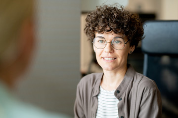 Young confident businesswoman looking at client or partner during interaction