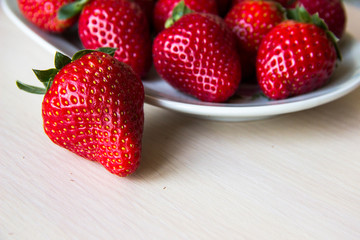 Fresh strawberries on a white plate on a wooden light background, copy space. Strawberry background. Sweet, juicy, ripe strawberries. Harvest of organic local  strawberries. Healthy food with vitamins
