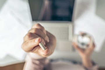 Top view. Tired business woman  holding a headache pill on the workplace with glass of water on the background of graphics and charts printed on the paper.