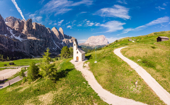 Beautifull aerial panoramic view to path to small white chapel San Maurizio and Dolomiti mountain landscape in background. Selva di Val Gardena, Bolzano, Trentino Alto Adige, Passo Sella, Italy