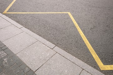 Asphalt texture at the bus stop with part of the curb and yellow stripe