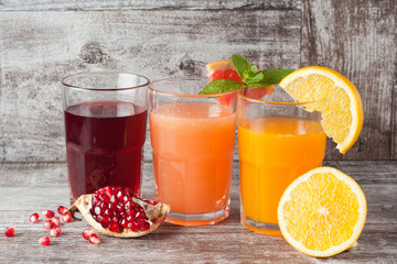 Glasses of pomegranate, grapefruit, orange juice on wooden background. Refreshments and summer...