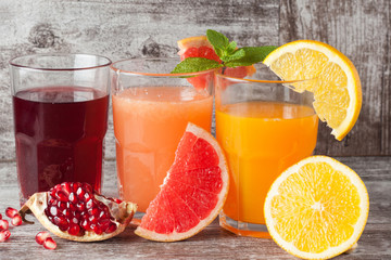 Glasses of pomegranate, grapefruit, orange juice on wooden background. Refreshments and summer drinks.