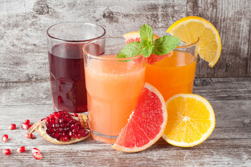 Glasses of pomegranate, grapefruit, orange juice on wooden background. Refreshments and summer drinks.