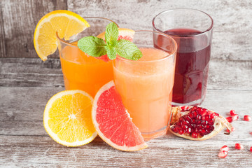 Glasses of pomegranate, grapefruit, orange juice on wooden background. Refreshments and summer drinks.