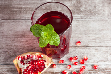 A glass of pomegranate juice with fresh pomegranate fruits on wooden table. Vitamins and minerals. Healthy drink concept.