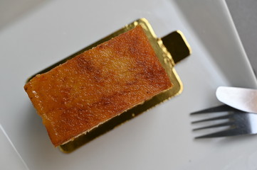A caramel cake on a white plate with a silver fork.