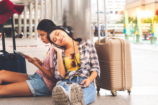 Asian women tourists, sitting on the train station, watching the tourist map and wearing headphones while waiting for the train, to summer concept.